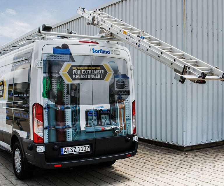 Eine Metallleiter wird mit einem Lift auf das Dach eines Transporters geladen